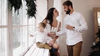 年轻可<strong>爱</strong>的<strong>一家人</strong>坐在装饰着圣诞花环的窗户旁。 <strong>爱</strong>的父母互相亲吻
